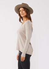 [Color: Heather Cement] A side facing image of a brunette model wearing a soft  knit pullover sweater in taupe. With a comfortable v neckline, long sleeves, and an open back with surplice accent. The perfect basic knit top for any season. 