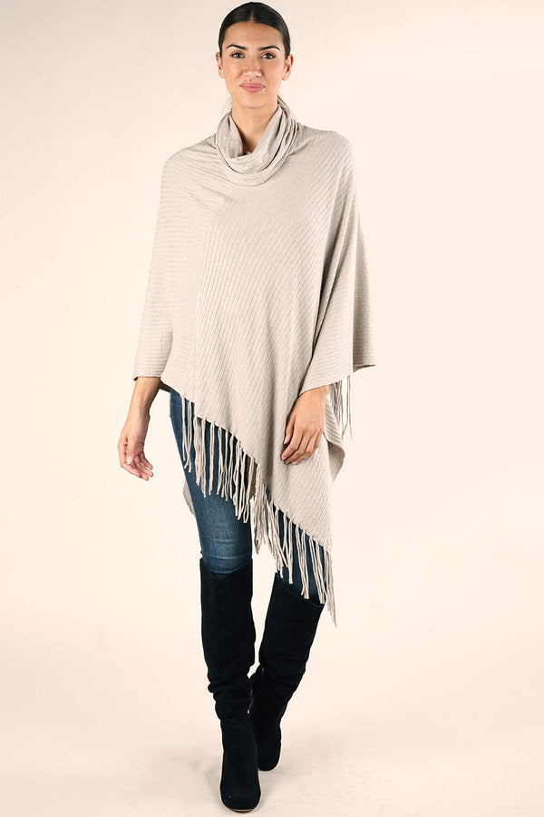 [Color: Heather Stone] A brunette model wearing a light beige cable knit rib sweater poncho. With a cowl neckline and an asymmetric fringed hemline.