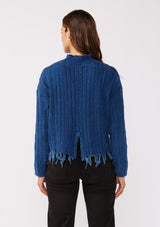 [Color: Indigo] A relaxed fit indigo blue cable knit sweater. A 100% cotton pullover featuring a fringed hemline, a mock neckline, and a back vent detail. Styled with dark denim for the Fall season. 