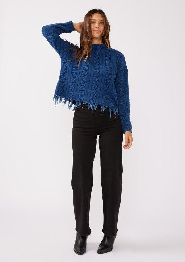 [Color: Indigo] A relaxed fit indigo blue cable knit sweater. A 100% cotton pullover featuring a fringed hemline, a mock neckline, and a back vent detail. Styled with dark denim for the Fall season. 