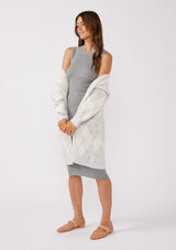 [Color: Heather Grey/Ivory] An image of a brunette model wearing an ultra-soft mid length cardigan in a light grey and ivory argyle plaid pattern. With long sleeves, an open front, and side pockets. Styled with a grey midi dress for a formal yet casual look. 