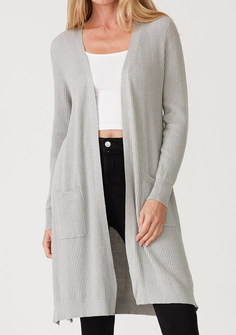 [Color: Heather Silver Grey] A detail front facing image of a blonde model wearing a light heather grey waffle knit cardigan. A lightweight mid length cardigan sweater with long sleeves, side pockets, and an open front. 