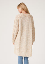 [Color: Oatmeal] A back facing image of a blonde model wearing an oatmeal chunky knit cardigan. A fall sweater with long sleeves, cable knit sleeve detail, an open front, and side pockets. 