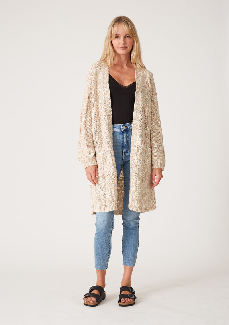 [Color: Oatmeal] A full body front facing image of a blonde model wearing an oatmeal chunky knit cardigan. A fall sweater with long sleeves, cable knit sleeve detail, an open front, and side pockets. 