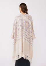 [Color: Oatmeal Multi] A back facing image of a brunette model wearing a fuzzy bohemian sweater poncho in a cream multi color knit. With an open front and tassel fringe trim. The perfect on the go style when an extra cozy layer is needed. Styled with a casual black maxi for the Fall season. 