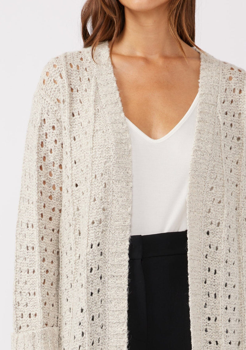 [Color: Oatmeal] A detailed image of a brunette model wearing an oatmeal open knit cardigan sweater. A mid length lightweight cardigan with long sleeves, an open front, and ribbed wrist cuffs.