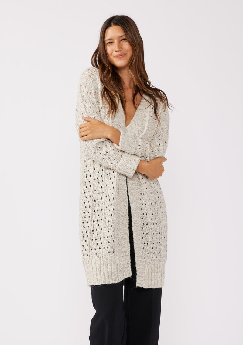 [Color: Oatmeal] A front facing image of a brunette model wearing an oatmeal open knit cardigan sweater. A mid length lightweight cardigan with long sleeves, an open front, and ribbed wrist cuffs.