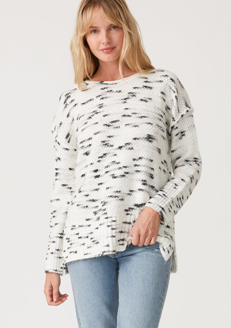 [Color: Ivory/Black] A front facing image of a blonde model wearing a black and white speckled knit pullover sweater. With long sleeves, exposed seam details, and a round neckline.