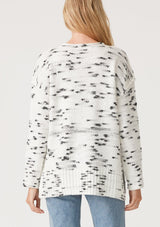 [Color: Ivory/Black] A back facing image of a blonde model wearing a black and white speckled knit pullover sweater. With long sleeves, exposed seam details, and a round neckline.