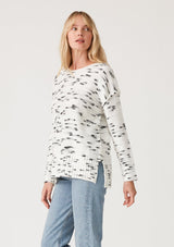 [Color: Ivory/Black] A side facing image of a blonde model wearing a black and white speckled knit pullover sweater. With long sleeves, exposed seam details, and a round neckline.