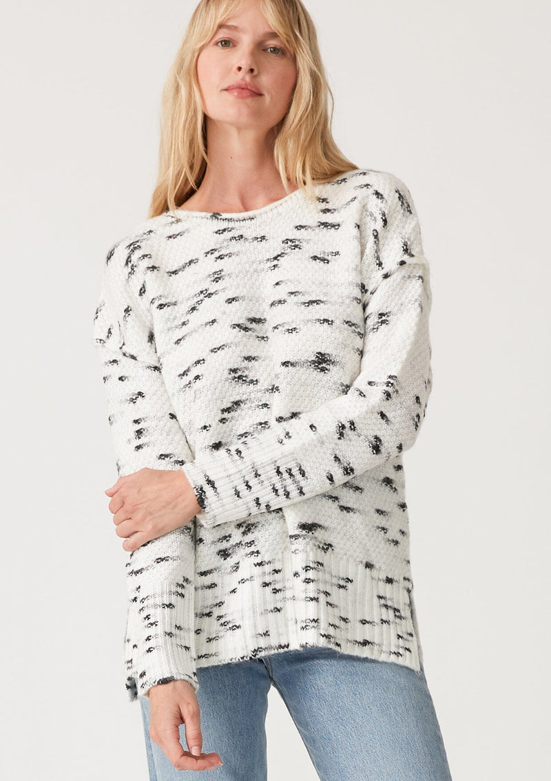 [Color: Ivory/Black] A front facing image of a blonde model wearing a black and white speckled knit pullover sweater. With long sleeves, exposed seam details, and a round neckline.