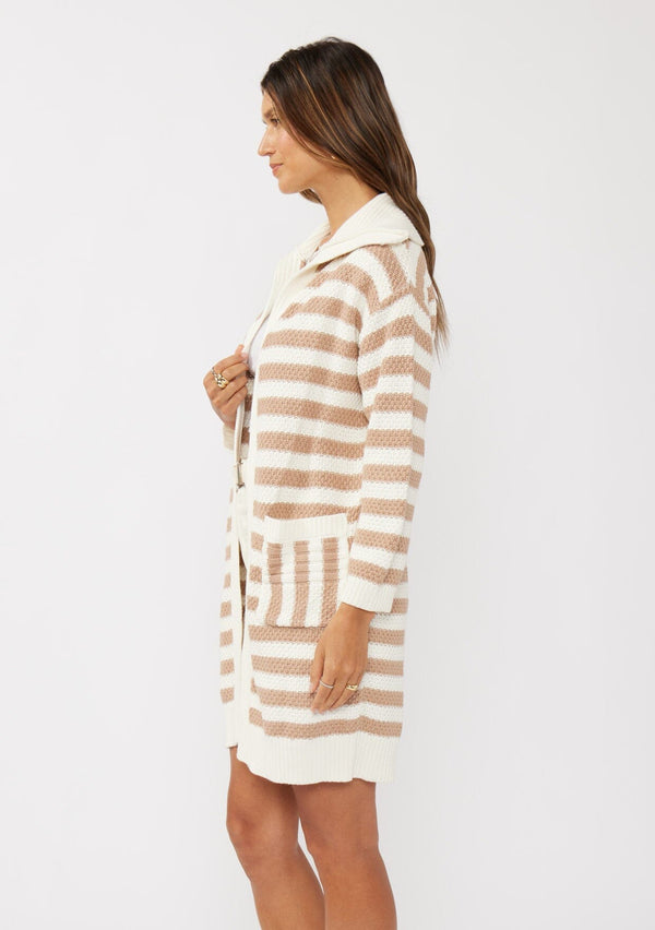 [Color: Natural/Taupe] A side facing image of a brunette model wearing a mid length cardigan in a natural and taupe stripe. With long sleeves, a collared neckline, an open front, and side pockets.