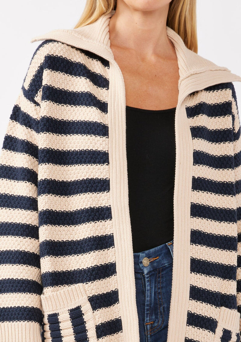 [Color: Navy/Natural] A detail image of a blonde model wearing a mid length cardigan in a black and white stripe. With long sleeves, a collared neckline, an open front, and side pockets.