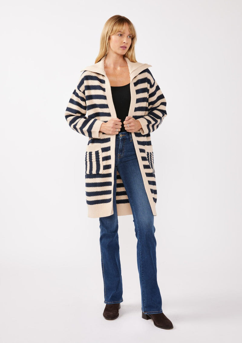 [Color: Navy/Natural] A back facing image of a blonde model wearing a mid length cardigan in a black and white stripe. With long sleeves, a collared neckline, an open front, and side pockets.