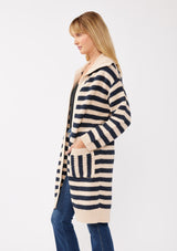 [Color: Navy/Natural] A side facing image of a blonde model wearing a mid length cardigan in a black and white stripe. With long sleeves, a collared neckline, an open front, and side pockets.