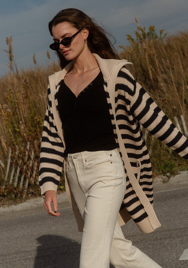 [Color: Navy/Natural] A front facing image of a brunette model wearing a mid length cardigan in a black and white stripe. With long sleeves, a collared neckline, an open front, and side pockets.