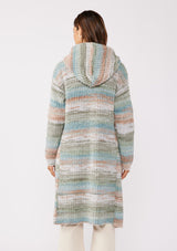 [Color: Mint/Natural] A back facing image with a brunette model wearing a cozy bohemian space dye chunky knit cardigan in a green mint multi-color stripe pattern. This plush cardigan features long sleeves, a cozy hood, essential pockets, and an open front. The long length and thick knit make it the perfect sweater for the fall season.