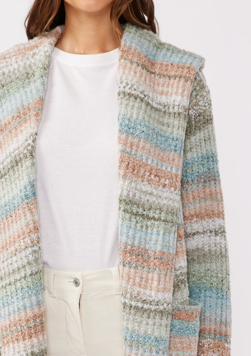 [Color: Mint/Natural] A detailed image with a brunette model wearing a cozy bohemian space dye chunky knit cardigan in a green mint multi-color stripe pattern. This plush cardigan features long sleeves, a cozy hood, essential pockets, and an open front. The long length and thick knit make it the perfect sweater for the fall season.