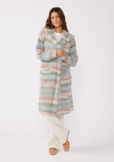 [Color: Mint/Natural] A front facing image with a brunette model wearing a cozy bohemian space dye chunky knit cardigan in a green mint multi-color stripe pattern. This plush cardigan features long sleeves, a cozy hood, essential pockets, and an open front. The long length and thick knit make it the perfect sweater for the fall season.