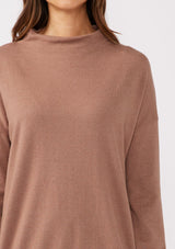 [Color: Chestnut] A detailed image of a brunette model wearing a brown cozy lightweight pullover with a mock neckline. Complete with long sleeves, dropped shoulders, and a snugged ribbed trim. Perfect for layering or styling on its own for a relaxed, laid-back fall look. 