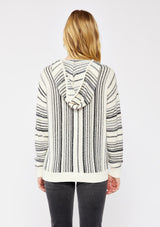 [Color: Natural/Black] A blonde model wearing a cozy striped sweater in ivory and black. A pullover sweater with long sleeves, v neckline, and ribbed cuffs and hem. Styled with black denim for an ultra cozy summer to fall look.