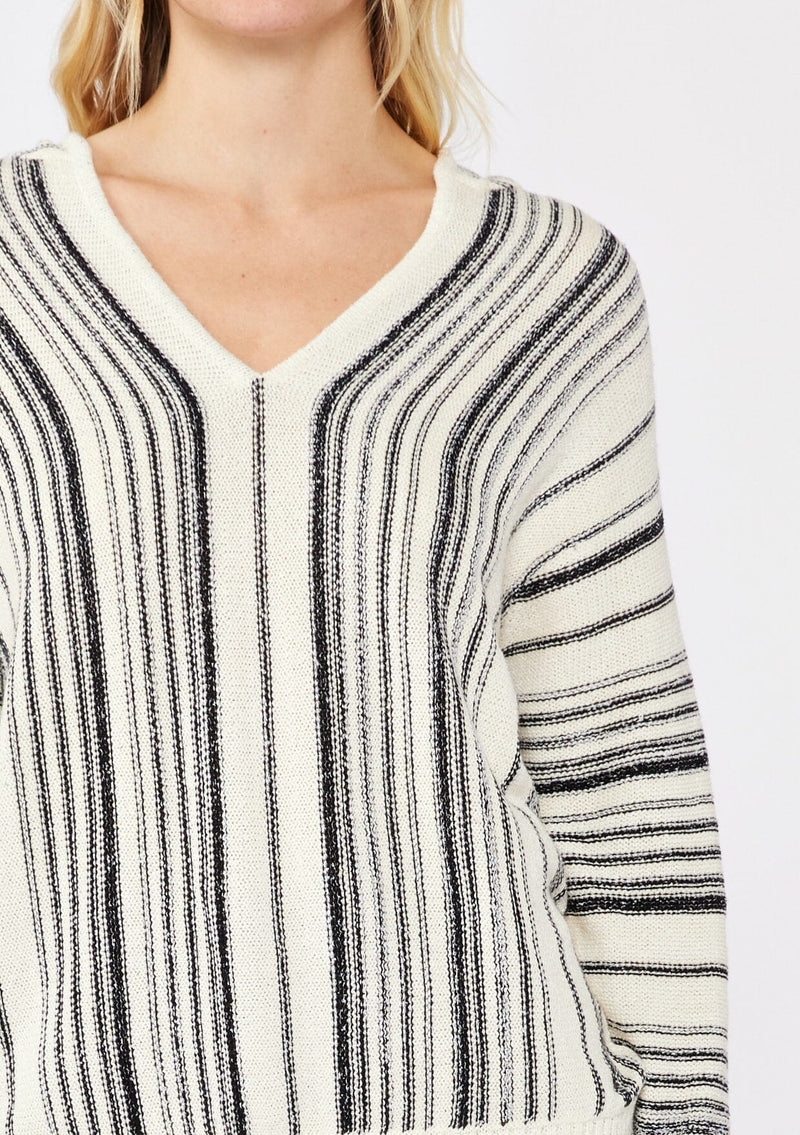 [Color: Natural/Black] A blonde model wearing a cozy striped sweater in ivory and black. A pullover sweater with long sleeves, v neckline, and ribbed cuffs and hem. Styled with black denim for an ultra cozy summer to fall look.