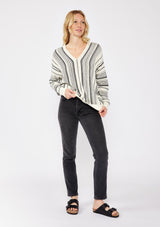 [Color: Natural/Black] A blonde model wearing a cozy striped sweater in ivory and black. A pullover sweater with long sleeves, v neckline, and ribbed cuffs and hem. Styled with black denim for an ultra cozy summer to fall look. 