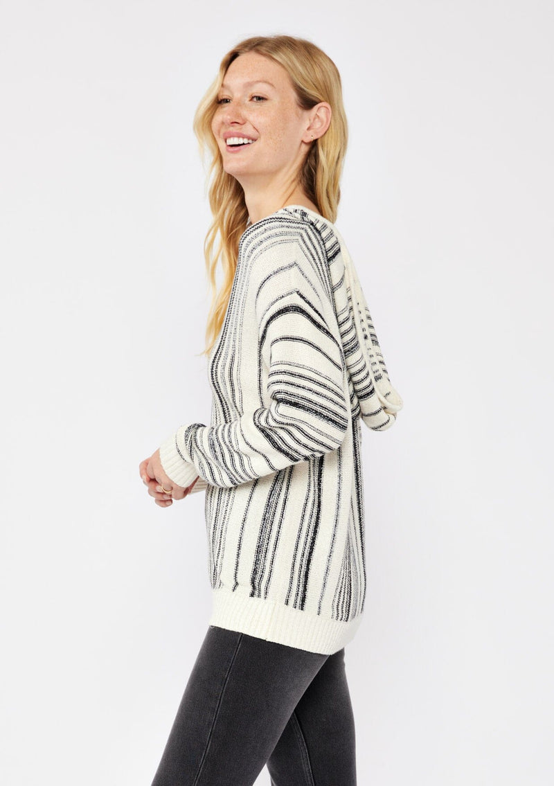 [Color: Natural/Black] A blonde model wearing a cozy striped sweater in ivory and black. A pullover sweater with long sleeves, v neckline, and ribbed cuffs and hem. Styled with black denim for an ultra cozy summer to fall look.