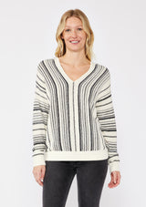 [Color: Natural/Black] A blonde model wearing a cozy striped sweater in ivory and black. A pullover sweater with long sleeves, v neckline, and ribbed cuffs and hem. Styled with black denim for an ultra cozy summer to fall look.