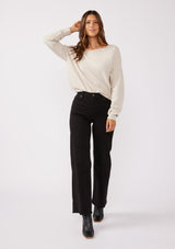 [Color: Heather Stone] A brunette model wearing a beige off white relaxed fit sweater with an asymmetrical neckline and long sleeves with a dropped shoulder. An everyday pullover sweater styled with dark denim jeans for the fall season.