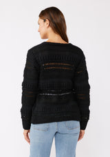 [Color: Black] A brunette model wearing a black sweater knit top with a wrap front and side tie closure. A chunky knit sweater with a mixed yarn weave and features an open knit design with a v neckline and long sleeves. 