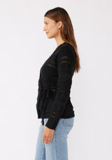 [Color: Black] A brunette model wearing a black sweater knit top with a wrap front and side tie closure. A chunky knit sweater with a mixed yarn weave and features an open knit design with a v neckline and long sleeves. 