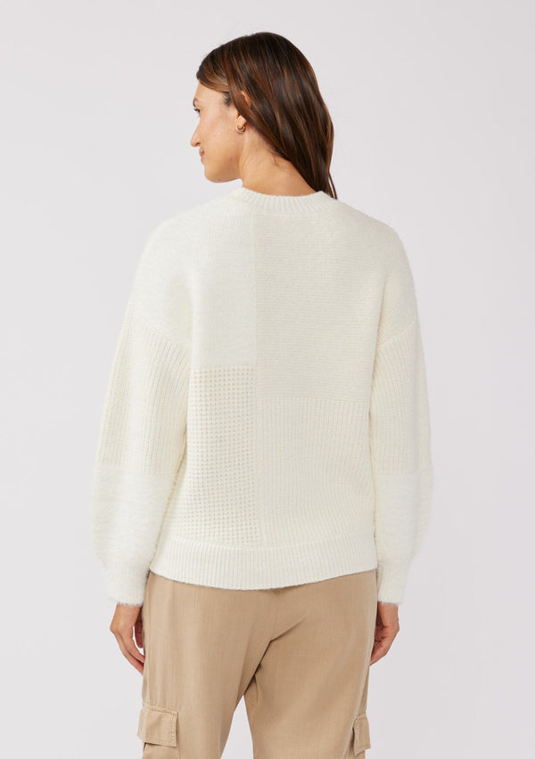 [Color: Cream] A brunette model wearing a fuzzy soft sweater crafted in a mixed media patchwork. With a crew neckline, long sleeves, and a relaxed fit. This cozy pullover sweater in cream ivory is the perfect addition to any Fall wardrobe. 