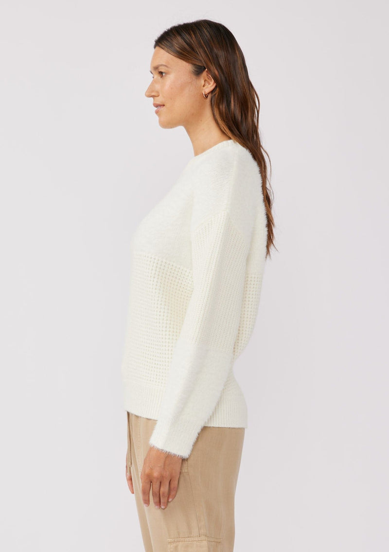 [Color: Cream] A brunette model wearing a fuzzy soft sweater crafted in a mixed media patchwork. With a crew neckline, long sleeves, and a relaxed fit. This cozy pullover sweater in cream ivory is the perfect addition to any Fall wardrobe. 