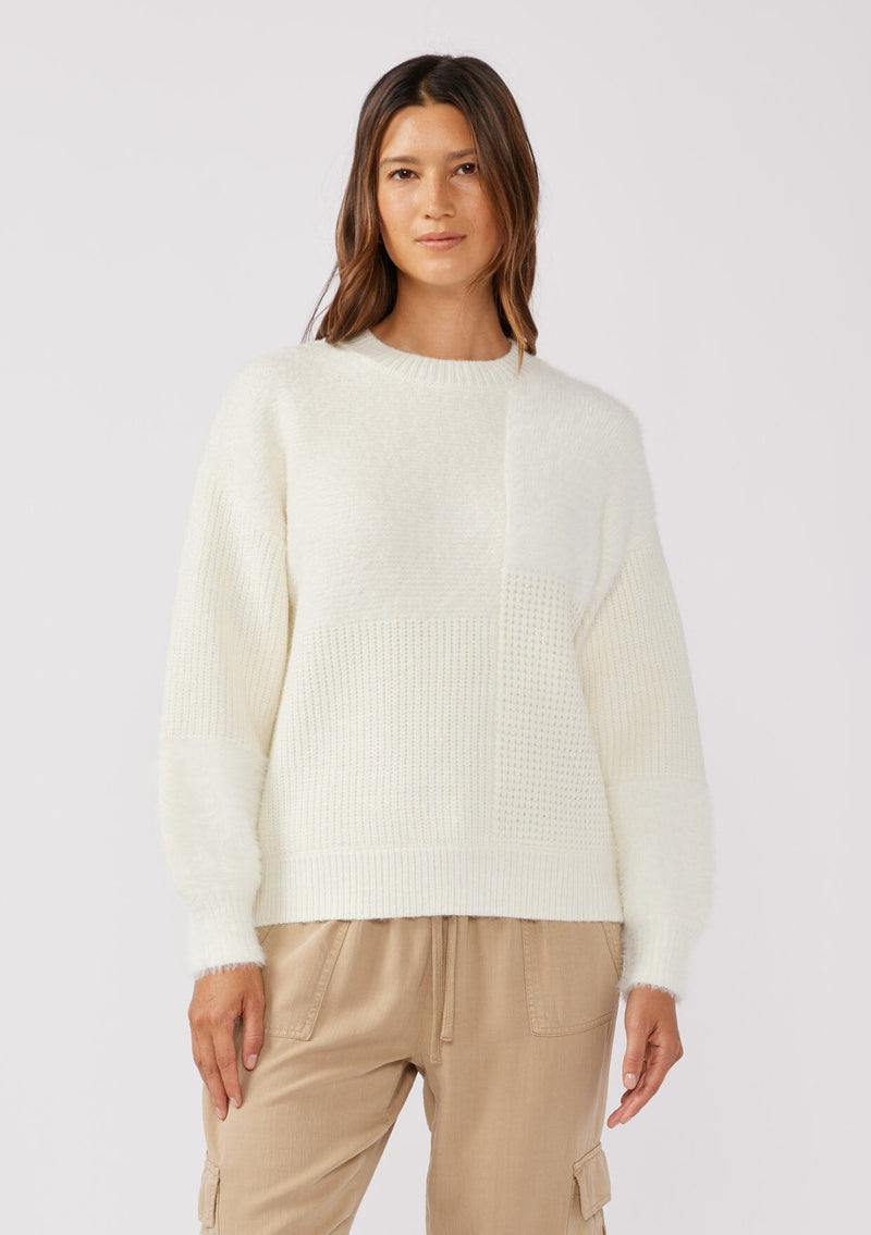 [Color: Cream] A brunette model wearing a fuzzy soft sweater crafted in a mixed media patchwork. With a crew neckline, long sleeves, and a relaxed fit. This cozy pullover sweater in cream ivory is the perfect addition to any Fall wardrobe. 