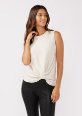 [Color: Vanilla] A front facing image of a brunette model wearing a cozy off white sweater tank top with a ribbed texture, twisted front hemline and a round neckline. A relaxed casual top for the spring season. 