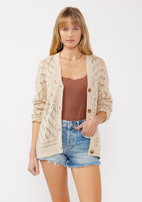 [Color: Vanilla] A front facing image of a blonde model wearing wearing a light 
beige pointelle cardigan with an open knit design, button front, v-neckline, long sleeves, and ribbed trim, ideal for versatile spring layering.