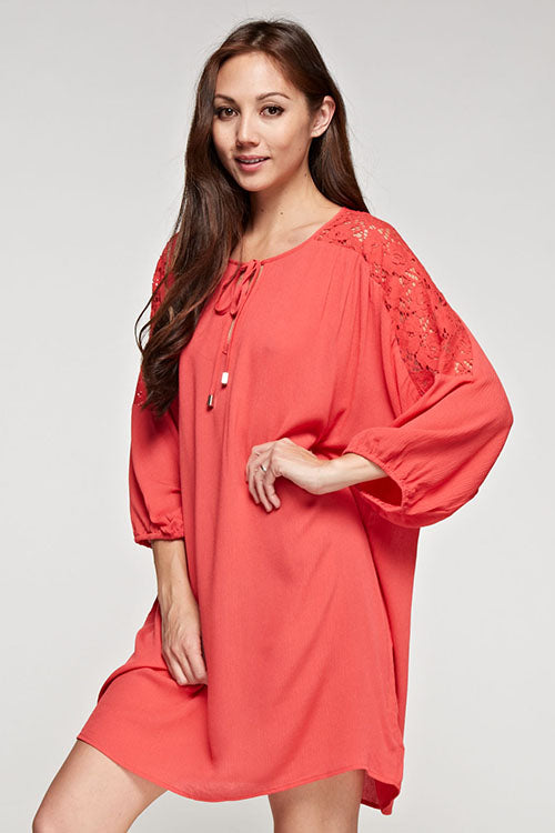 [Color: Poppy] A brunette model wearing a coral relaxed-fit mini dress with long sleeves, elastic cuffs, lace shoulder accents, and a split V-neckline with tie detail—a breezy beach cover-up.