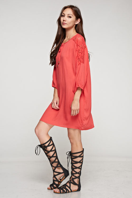 [Color: Poppy] A brunette model wearing a coral relaxed-fit mini dress with long sleeves, elastic cuffs, lace shoulder accents, and a split V-neckline with tie detail—a breezy beach cover-up.