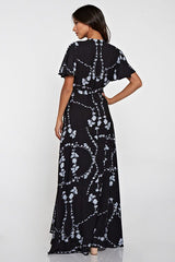 [Color: Black Combo] A black facing image of a brunette model wearing a  black flowy wrap dress with a floral print. A boho dress with a short flutter sleeves, surplice v-neckline, and a side tie waist closure. 