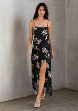 [Color: Black/Red] A brunette model wearing a black dress with a red floral design. A slit maxi dress with a scoop neckline, adjustable spaghetti straps, and lattice trims. A versatile dress for day to night.