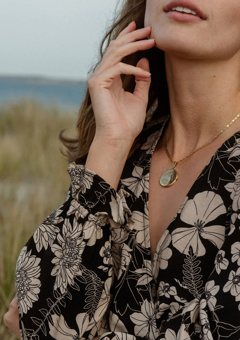 [Color: Black/Taupe] A detail image of a brunette model wearing a black and taupe floral print mini dress near the ocean. This casual boho style features a surplice v-neckline, long sleeves with ruffled cuffs, and a flowy tiered skirt. Ideal for casual brunch outings, vacations, and special occasions.