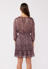 [Color: Black/Plum] A back facing image of a brunette model wearing a purple floral print mini dress with shimmering metallic stripes. This holiday dress features a flattering v-neckline, 3/4 length sleeves, a smocked waist, and a ruffle-trimmed skirt. Ideal for special occasions and festive events.