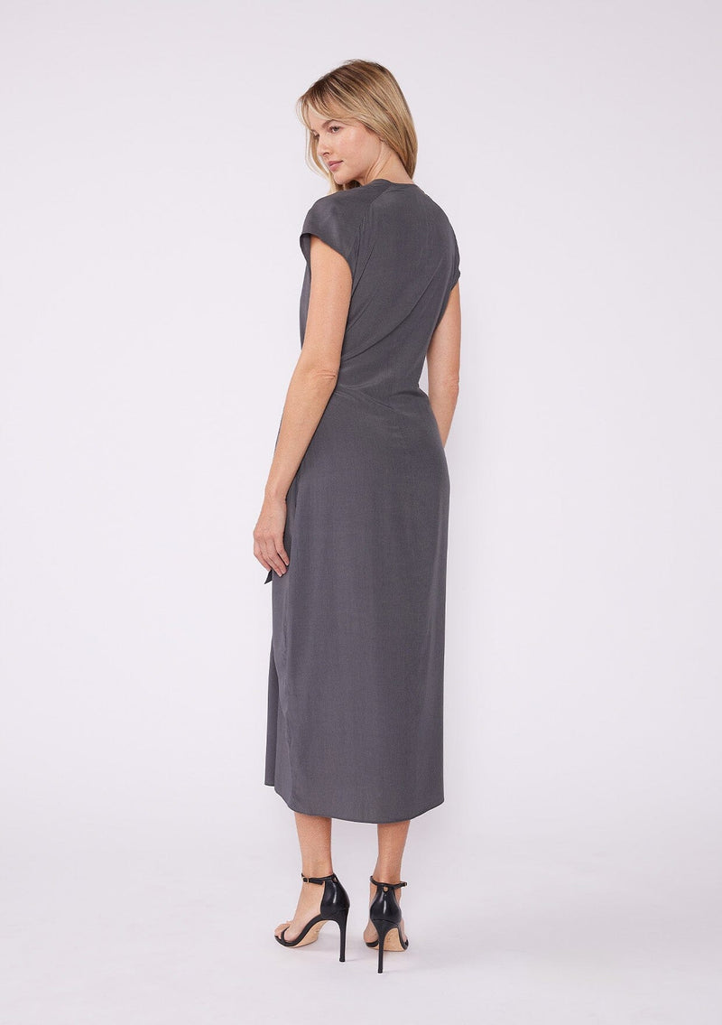 [Color: Pewter] A front facing image of a blonde model wearing a dark grey pewter maxi length wrap dress. With short cap sleeves, a deep v neckline, and a side tie waist closure. A beautiful office dress.