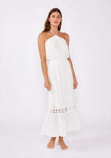 [Color: Off White] A brunette model wearing a white ultra bohemian maxi dress for vacation. This summer maxi dress features a halter neckline and a comfortable smocked waist. This dress is also embellished with intricate lace details and embroidered eyelet. The perfect style for brunch or a tropical vacation.