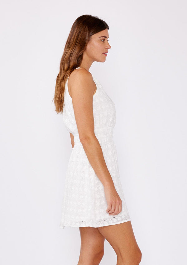 [Color: White] A brunette model wearing a white mini dress with a delicate embroidered floral through out. With a sleeveless design, surplice v neckline, and a double elastic waistline. A casual mini dress that can be worn to a brunch or special wedding occasions.