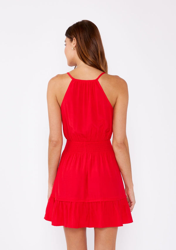 [Color: Poppy Red] A brunette woman wearing a casual bright red mini dress with a sleeveless design, split v neckline, smocked waistline, and a ruffle trimmed hem. A casual yet formal dress perfect for date night and special occasions.