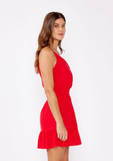 [Color: Poppy Red] A brunette woman wearing a casual bright red mini dress with a sleeveless design, split v neckline, smocked waistline, and a ruffle trimmed hem. A casual yet formal dress perfect for date night and special occasions.