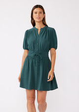 [Color: Dusty Teal] A front image of a brunette model wearing a classic Fall bohemian mini dress in a green teal. Crafted with a rayon and linen blend, this modern button front mini dress features short puff sleeves, a button front, and two adjustable drawstrings. 