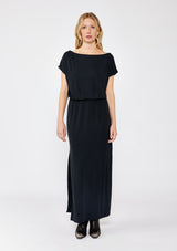 [Color: Black] A blonde model wearing a relaxed fit maxi that can be worn on or off shoulder. A casual black dress with a boat neckline, short dolman sleeves, elastic waistline, and side slits. Styled with black western boots for the fall season.